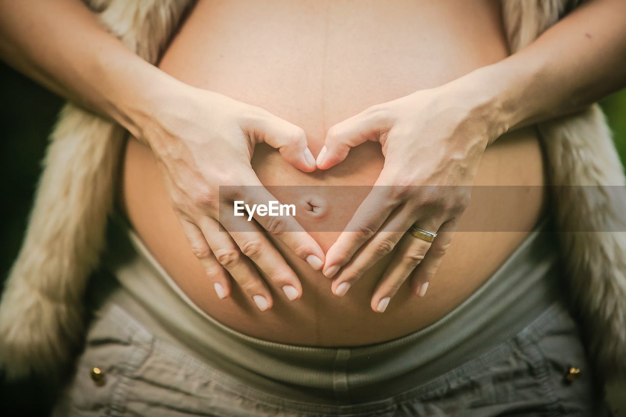 Midsection of pregnant woman with man hands making heart shape over abdomen