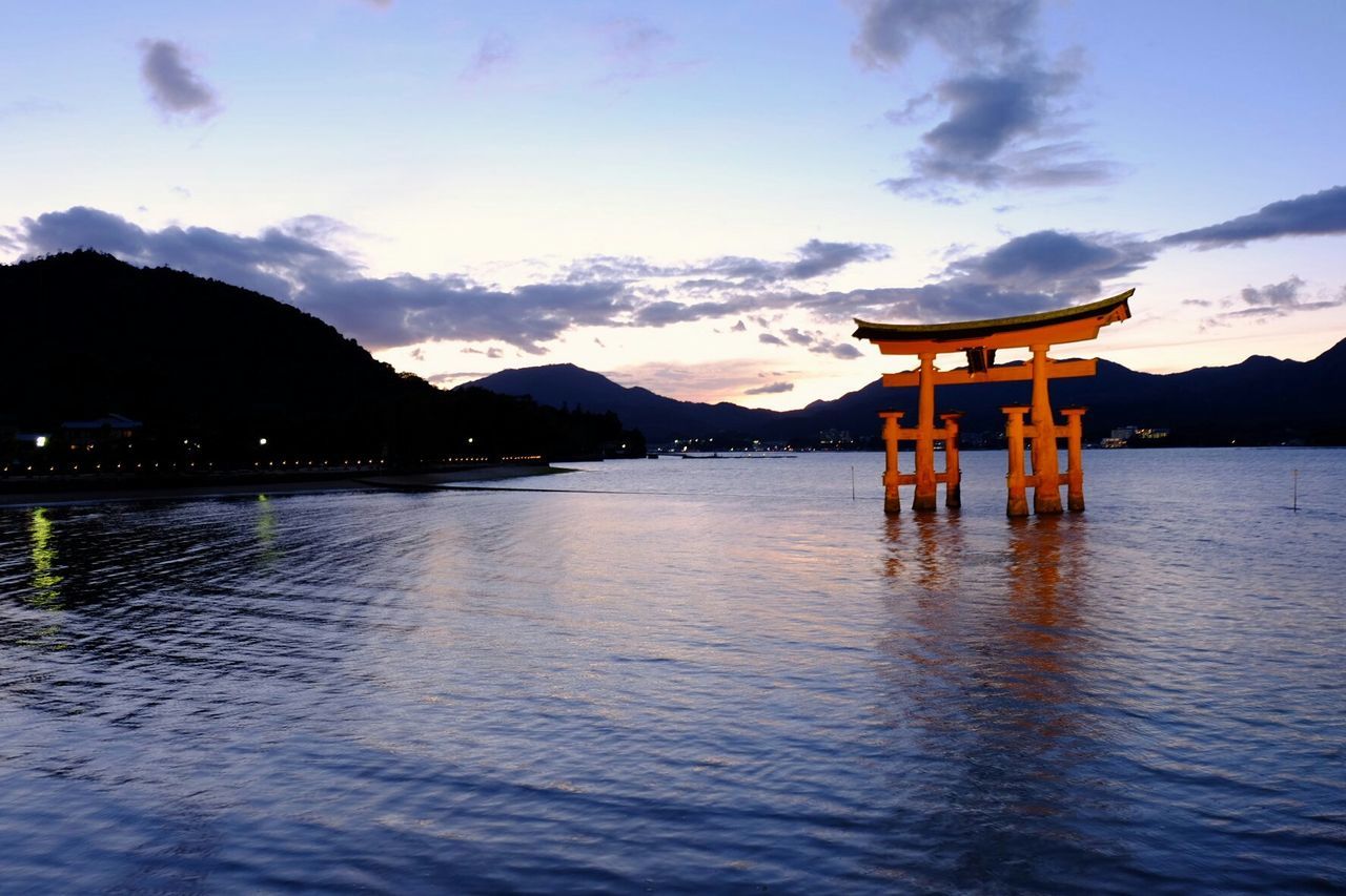 Itsukushima shrine in lake against sky during sunset