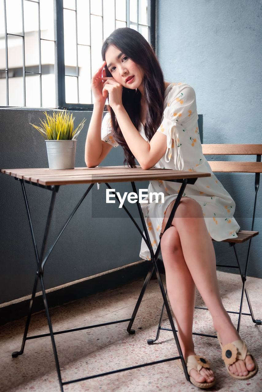 YOUNG WOMAN USING MOBILE PHONE WHILE SITTING ON CHAIR IN OFFICE