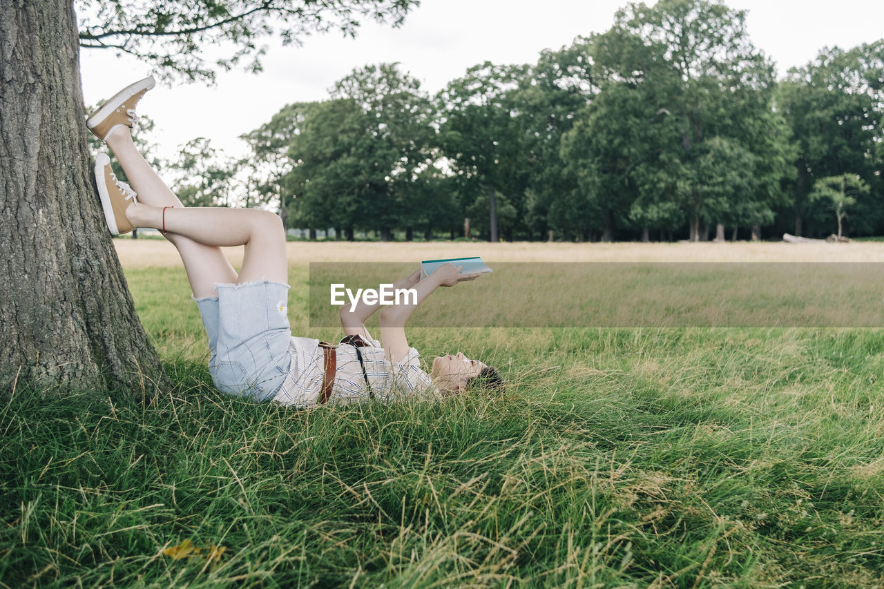 Woman reading book while relaxing on grass at park