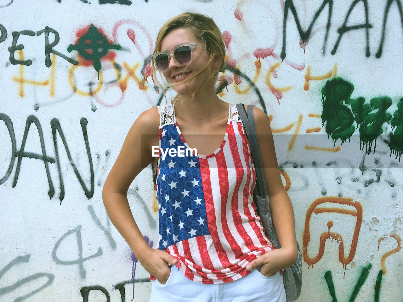 Young woman wearing american flag tank top while standing against graffiti wall