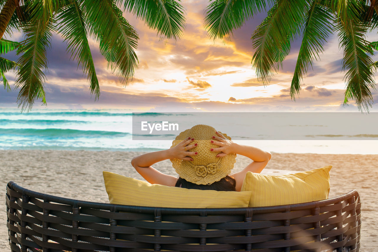 Rear view of woman relaxing on chair at beach