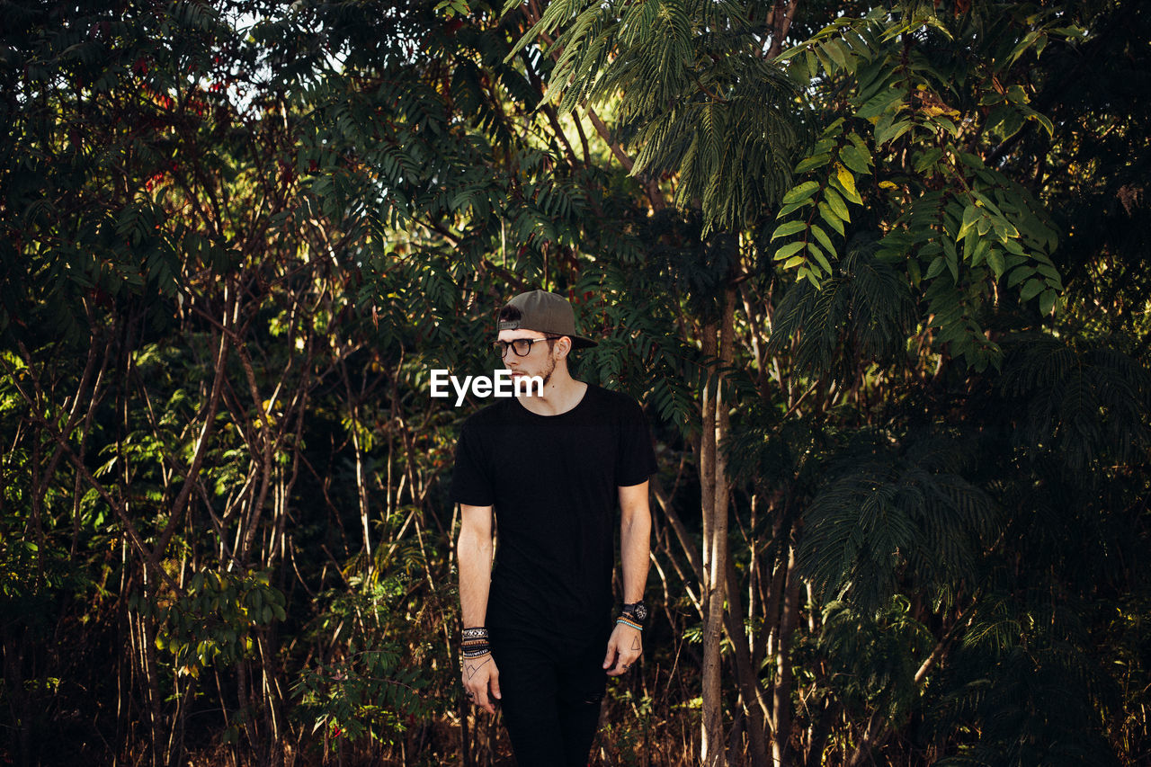 Young man standing amidst trees at forest