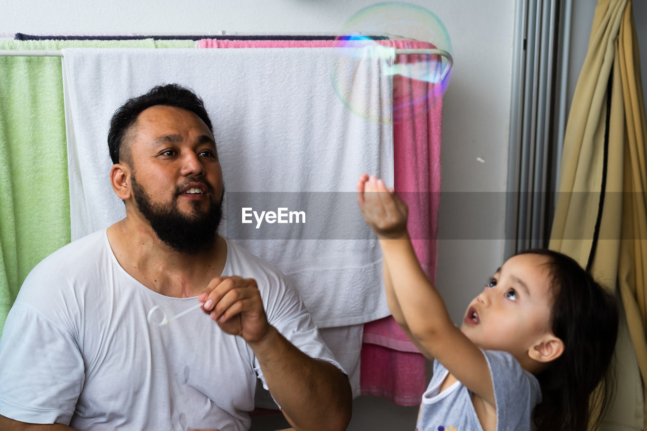 Father blowing bubbles with daughter at home