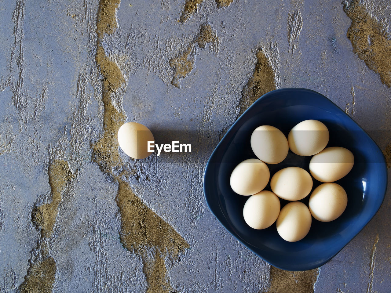 Flat lay photo of bowl with chicken eggs on blue background