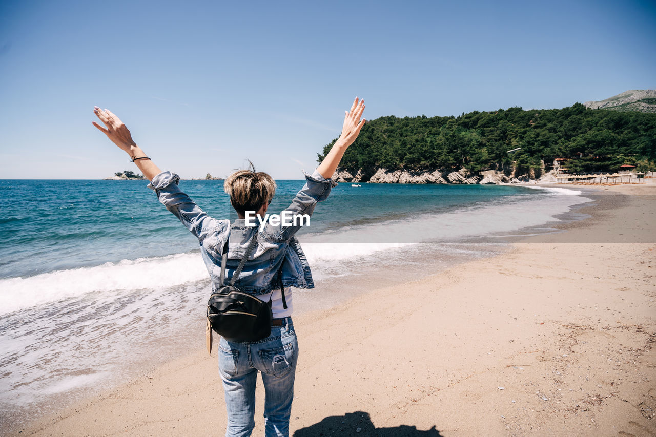 Girl with backpack on beach hands up person