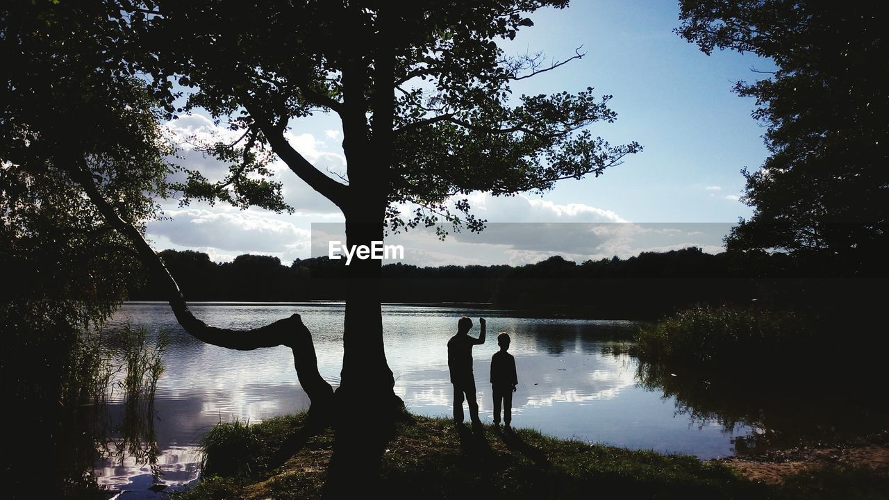 Silhouette boys standing at lakeshore