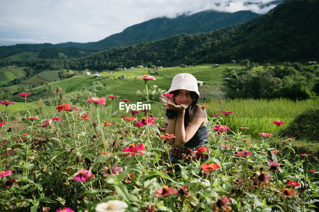 plant, meadow, flower, hat, nature, field, flowering plant, one person, mountain, landscape, beauty in nature, land, adult, environment, sun hat, growth, fashion accessory, women, rural scene, freshness, clothing, rural area, wildflower, grassland, sky, agriculture, mountain range, scenics - nature, day, green, leisure activity, portrait, lifestyles, outdoors, female, cloud, grass, summer, person, farm, poppy, red, occupation, young adult, plain, hiking, crop, three quarter length, tranquility, sunlight, relaxation