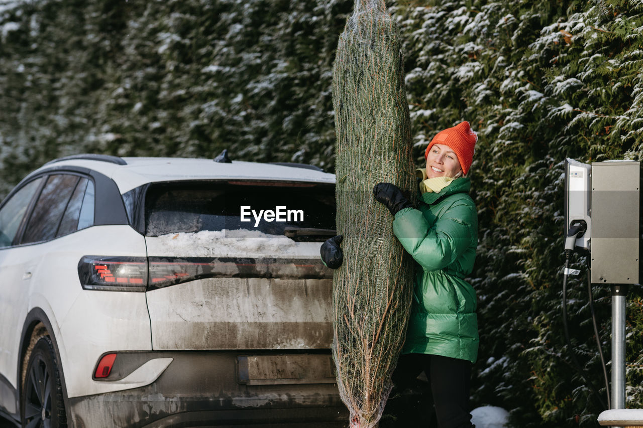 Smiling woman standing with christmas tree near car