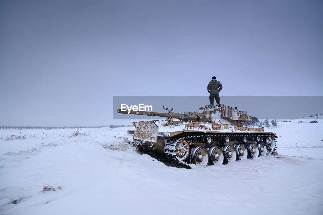 A tank in the snow with one of it crew members standing on it 