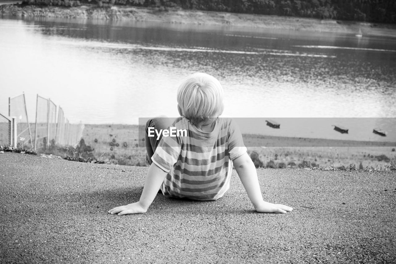 Rear view of boy sitting at lakeshore