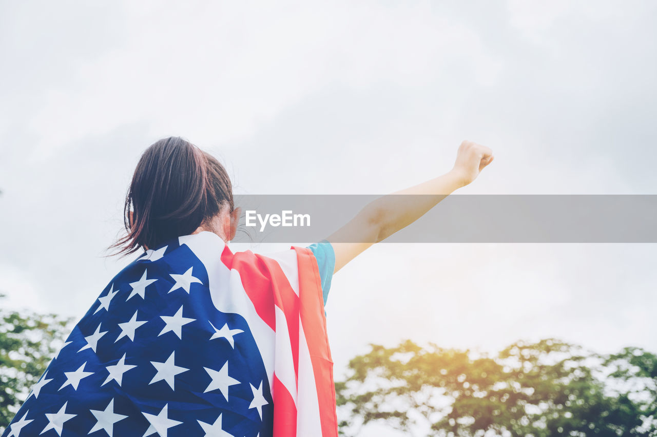 Low angle view of girl with american flag standing against sky