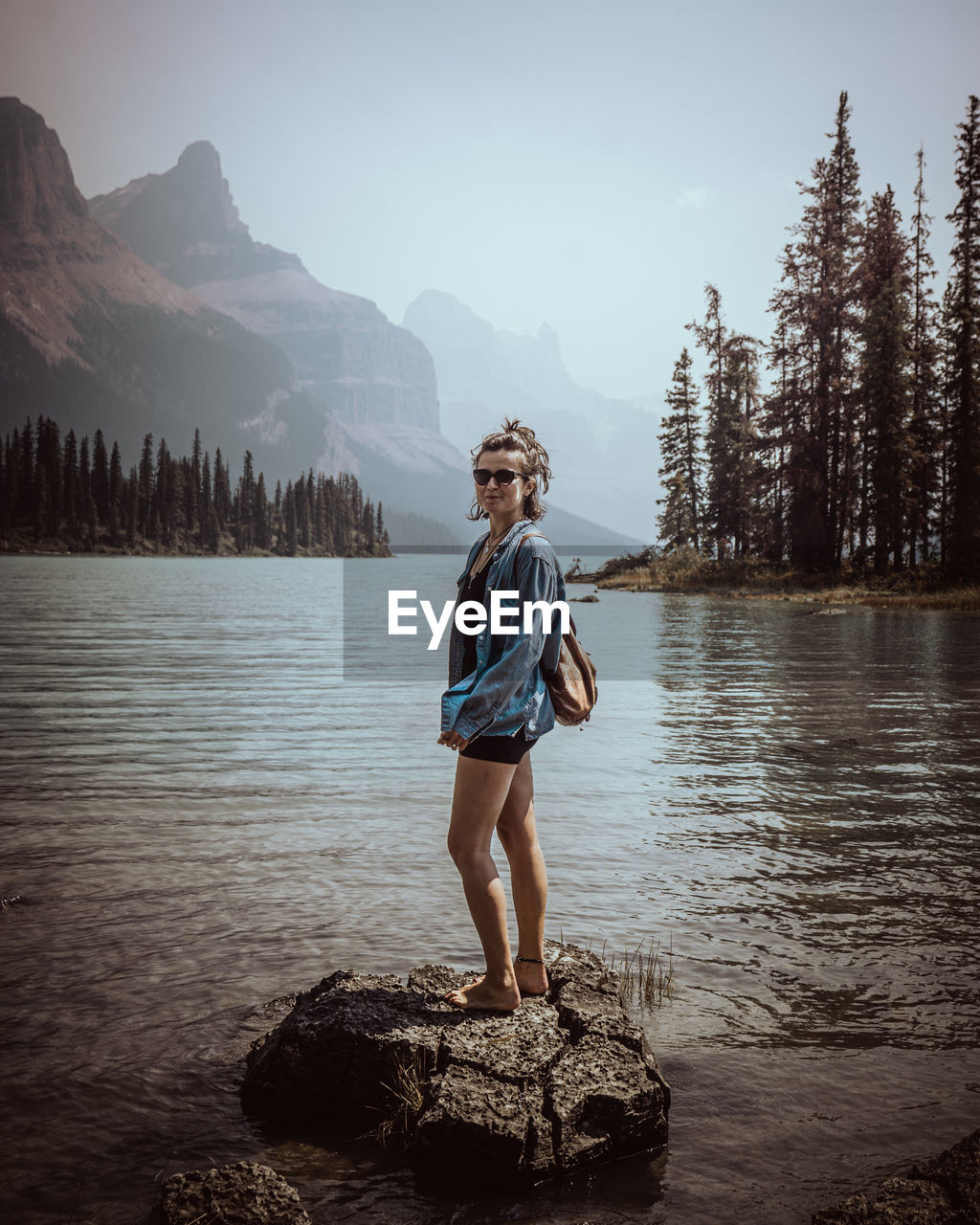Full length of girl standing on rock by lake against sky