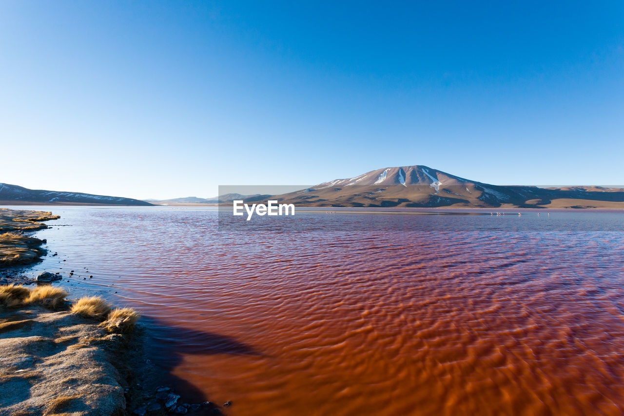 SCENIC VIEW OF SEA BY MOUNTAINS AGAINST CLEAR BLUE SKY