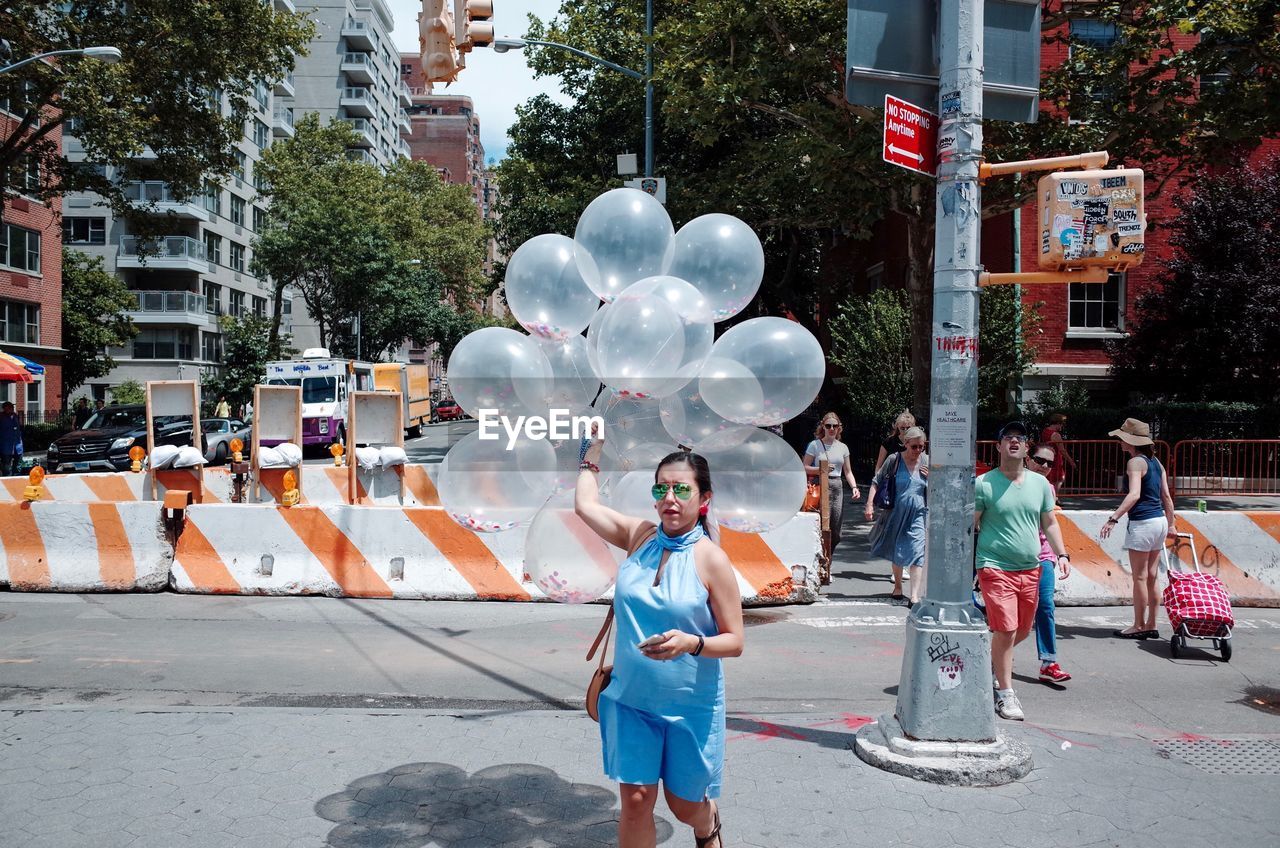 PORTRAIT OF YOUNG WOMAN WITH BALLOONS STANDING AGAINST BUILDINGS