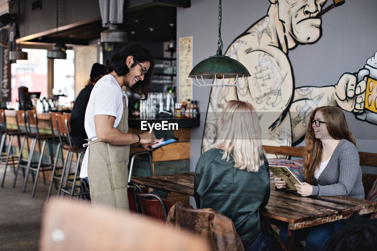 Smiling owner receiving order on digital tablet from customers at restaurant