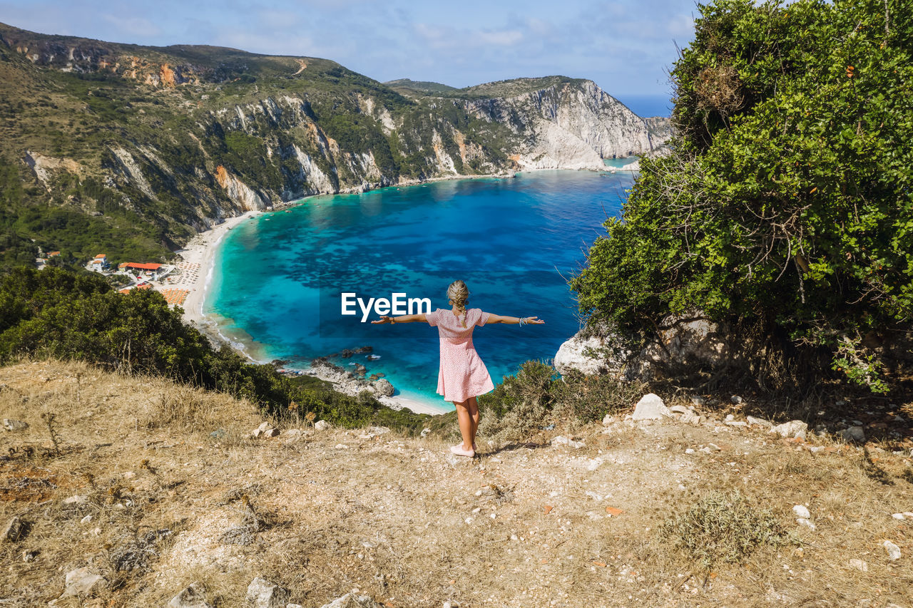 MAN STANDING ON SHORE BY MOUNTAINS