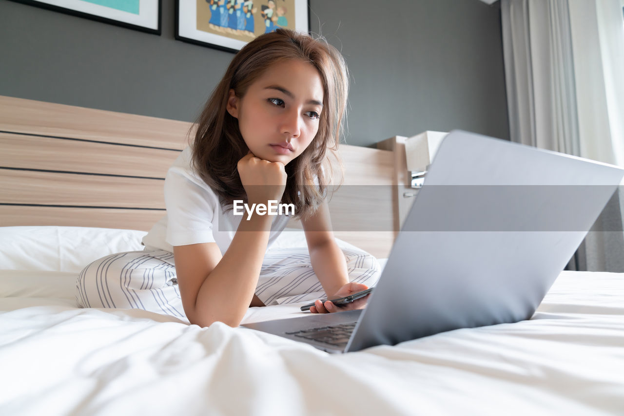 YOUNG WOMAN USING LAPTOP ON BED