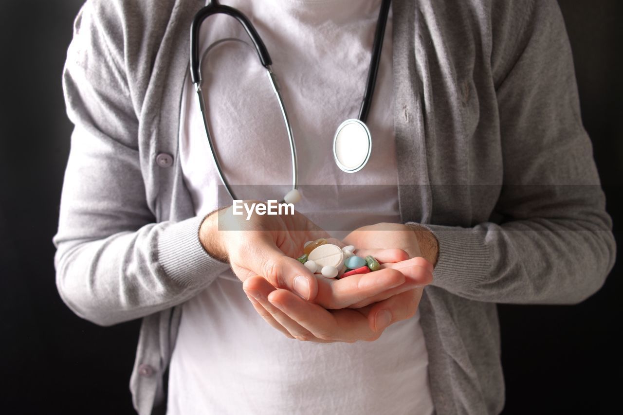 Midsection of doctor holding pills against black background