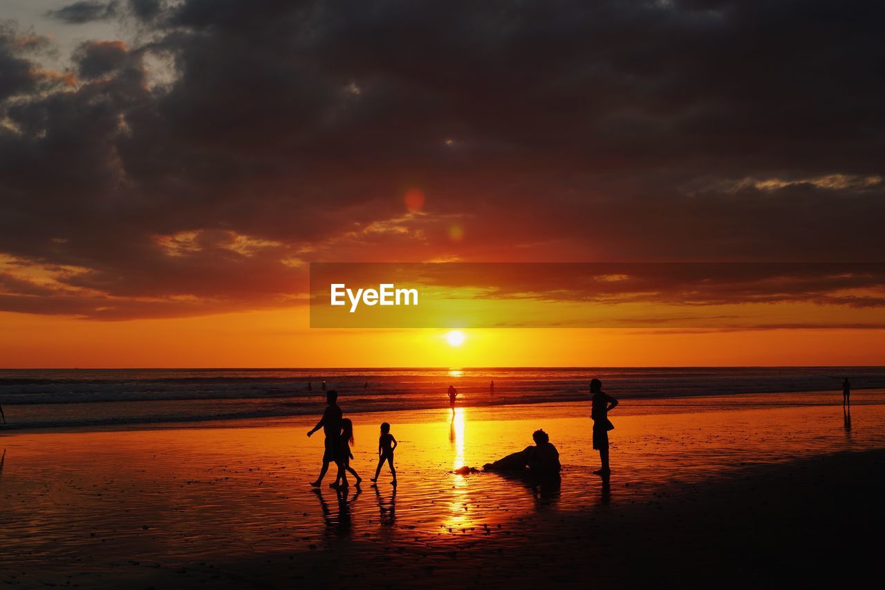 Silhouette people at beach against cloudy sky during sunset