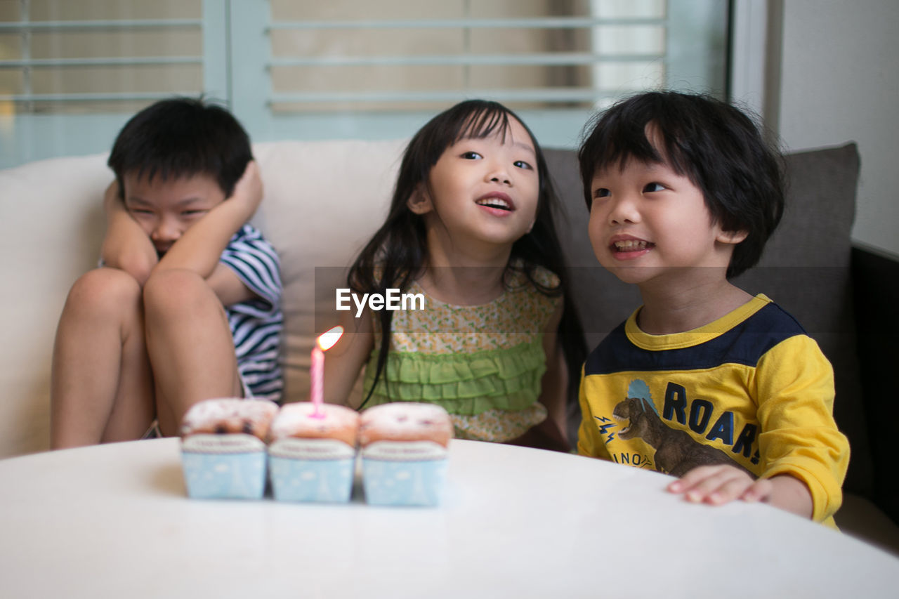 Children sitting by table with illuminated candle on cupcake