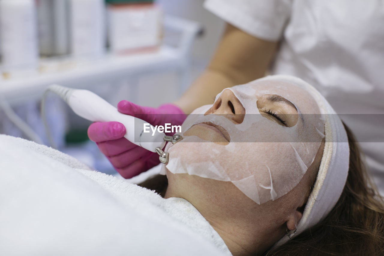 Woman with sheet mask getting beauty treatment in salon