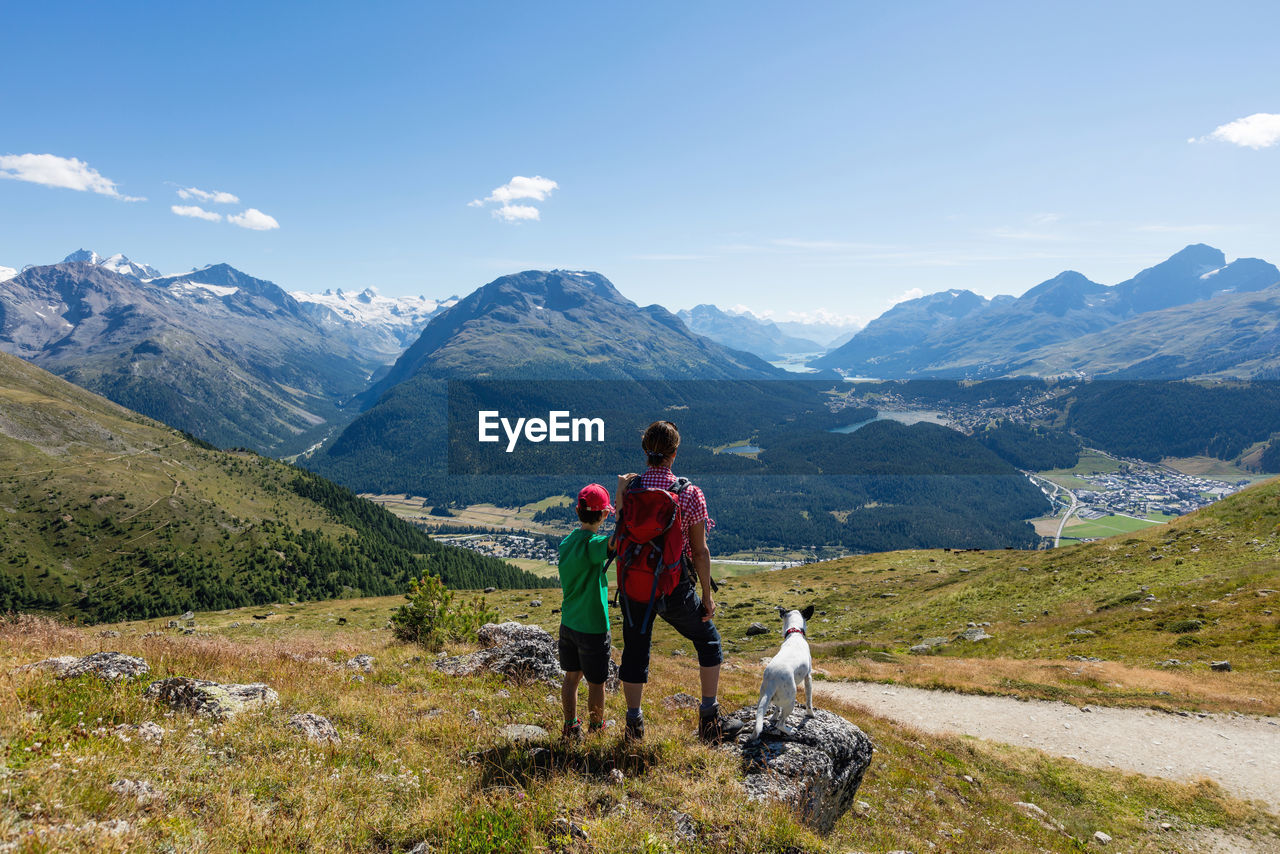 Rear view of people with dog on mountain against sky