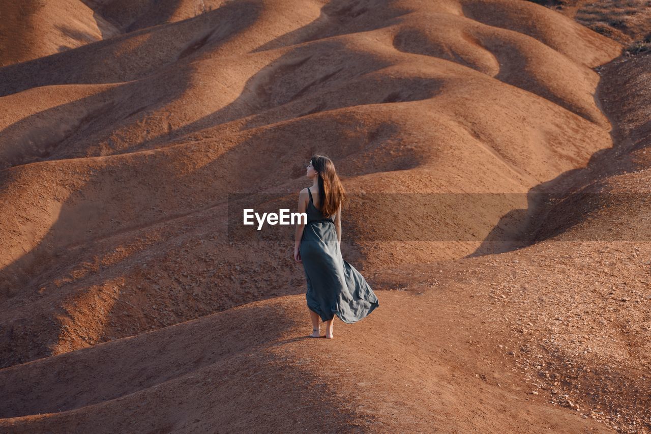 Rear view of woman walking on sand dune in desert