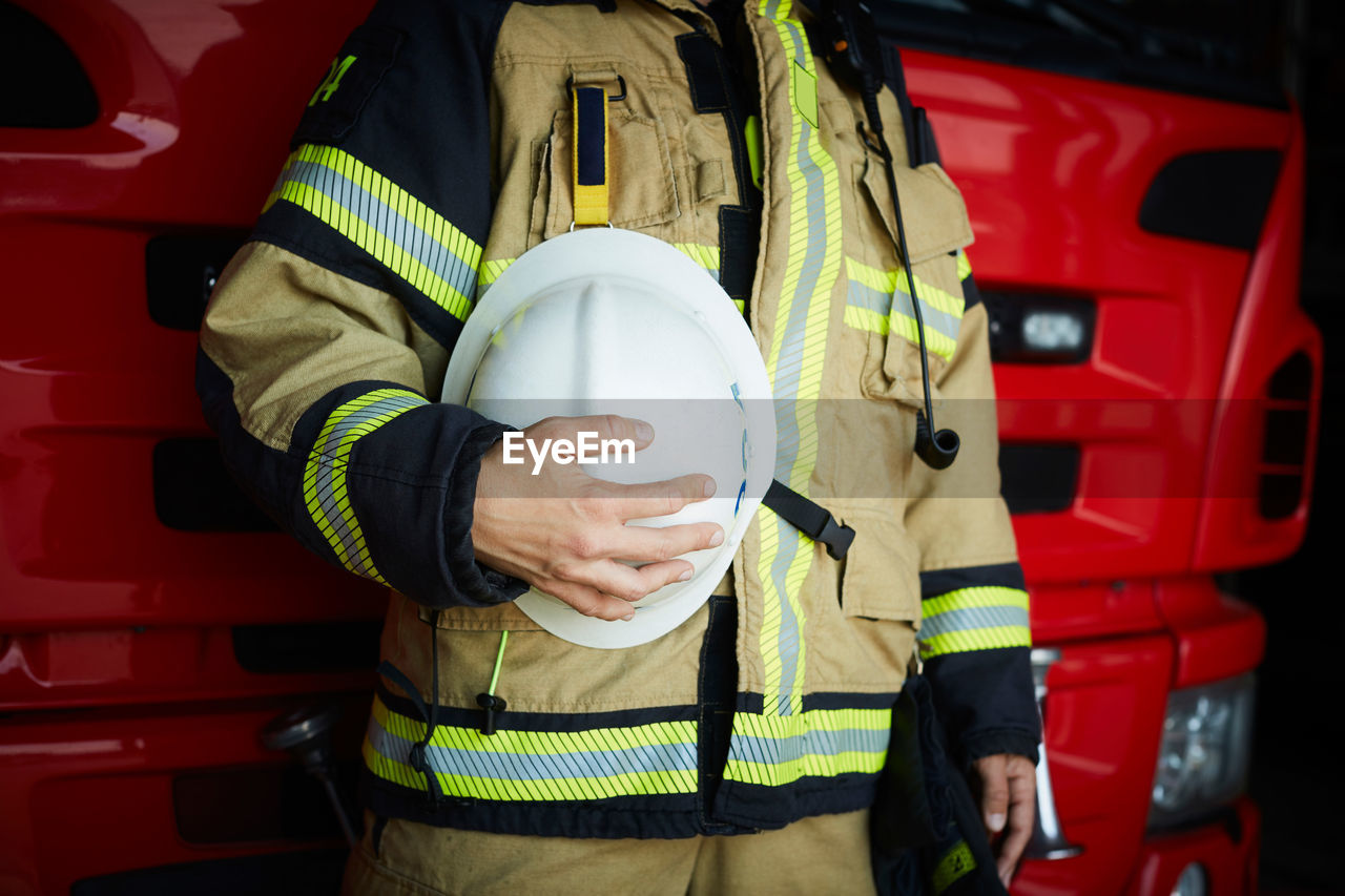 Midsection of female firefighter holding helmet while standing at fire station