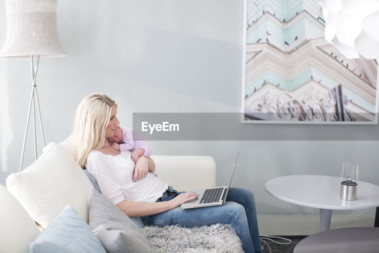 Woman holding newborn daughter and using laptop