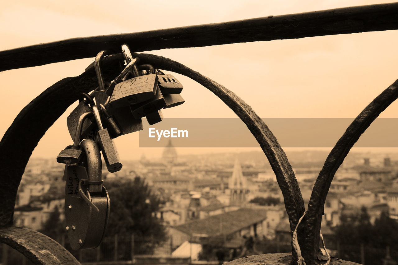 Close-up of padlocks hanging on railing against sky in city