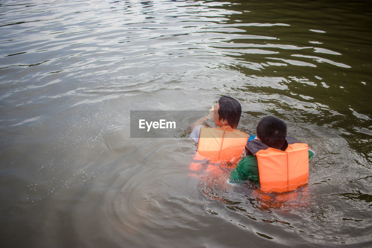 Rear view of man and boy swimming in river with life jacket