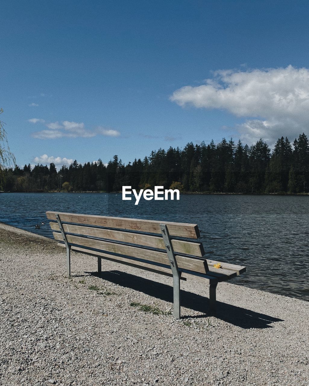 EMPTY BENCH ON LAKE AGAINST SKY