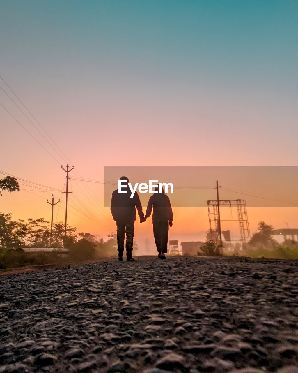 Rear view of couple walking on road during sunset