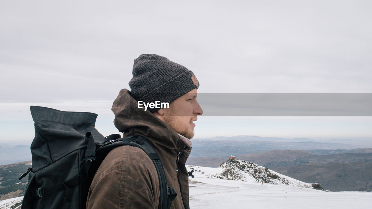 Male hiker standing on snow covered mountain against sky