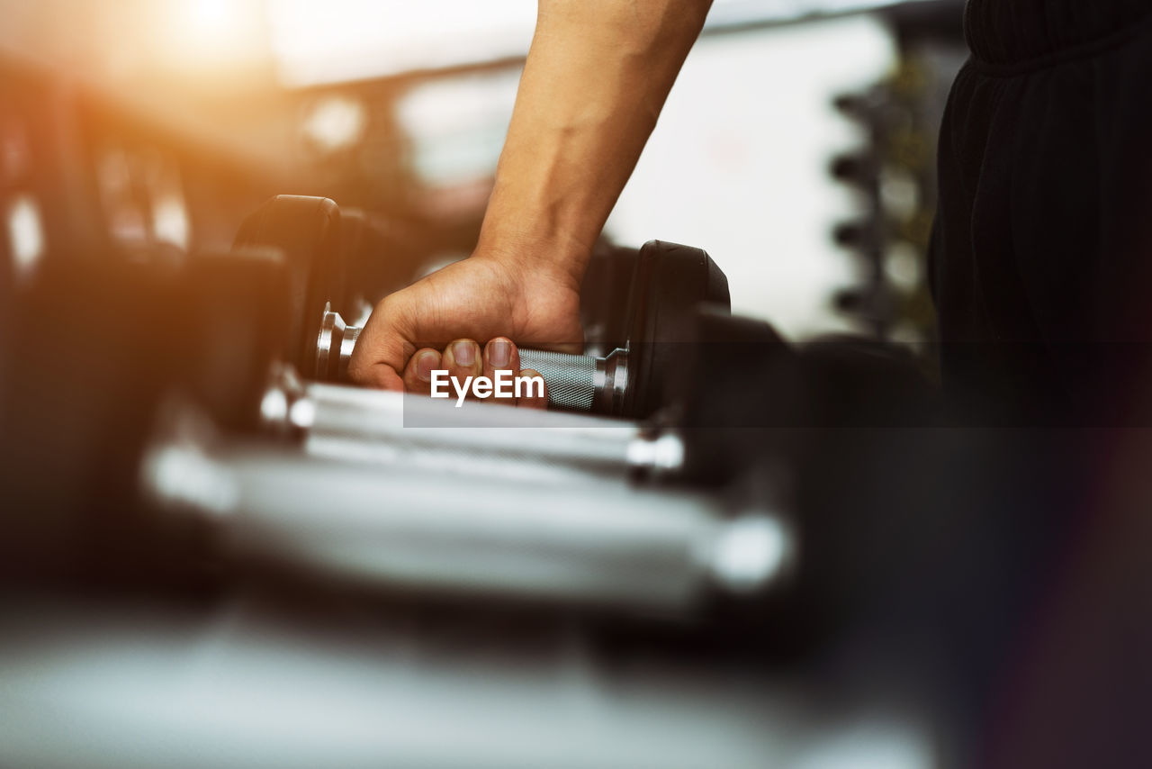 Cropped hand of man picking barbell at gym