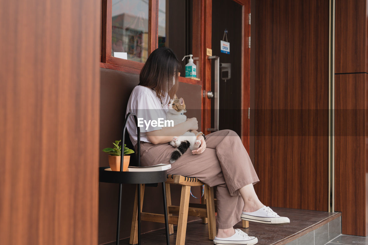 Asian woman wearing protective mask sit and play with her cat at outdoor coffee shop