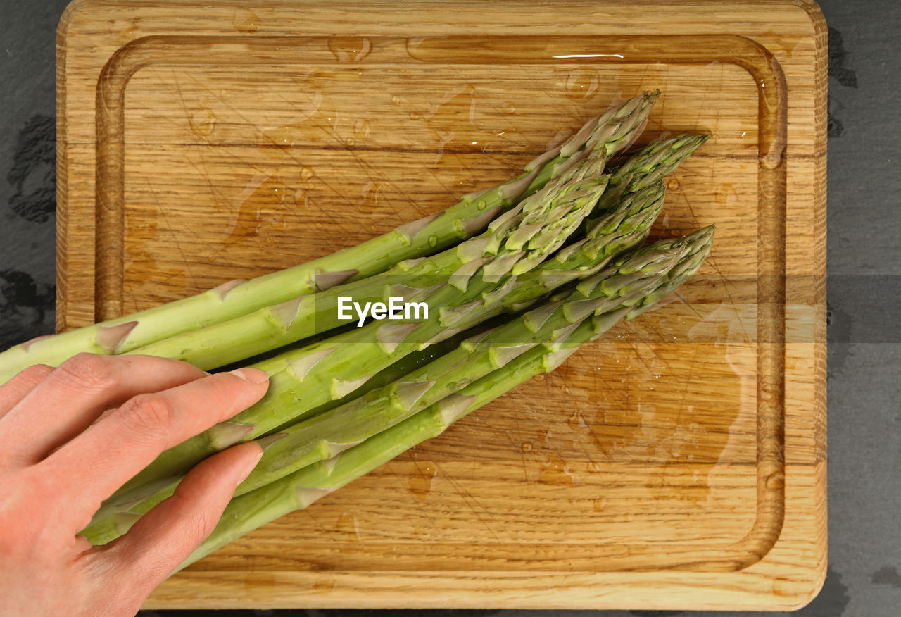 Cropped hand holding asparagus on cutting board