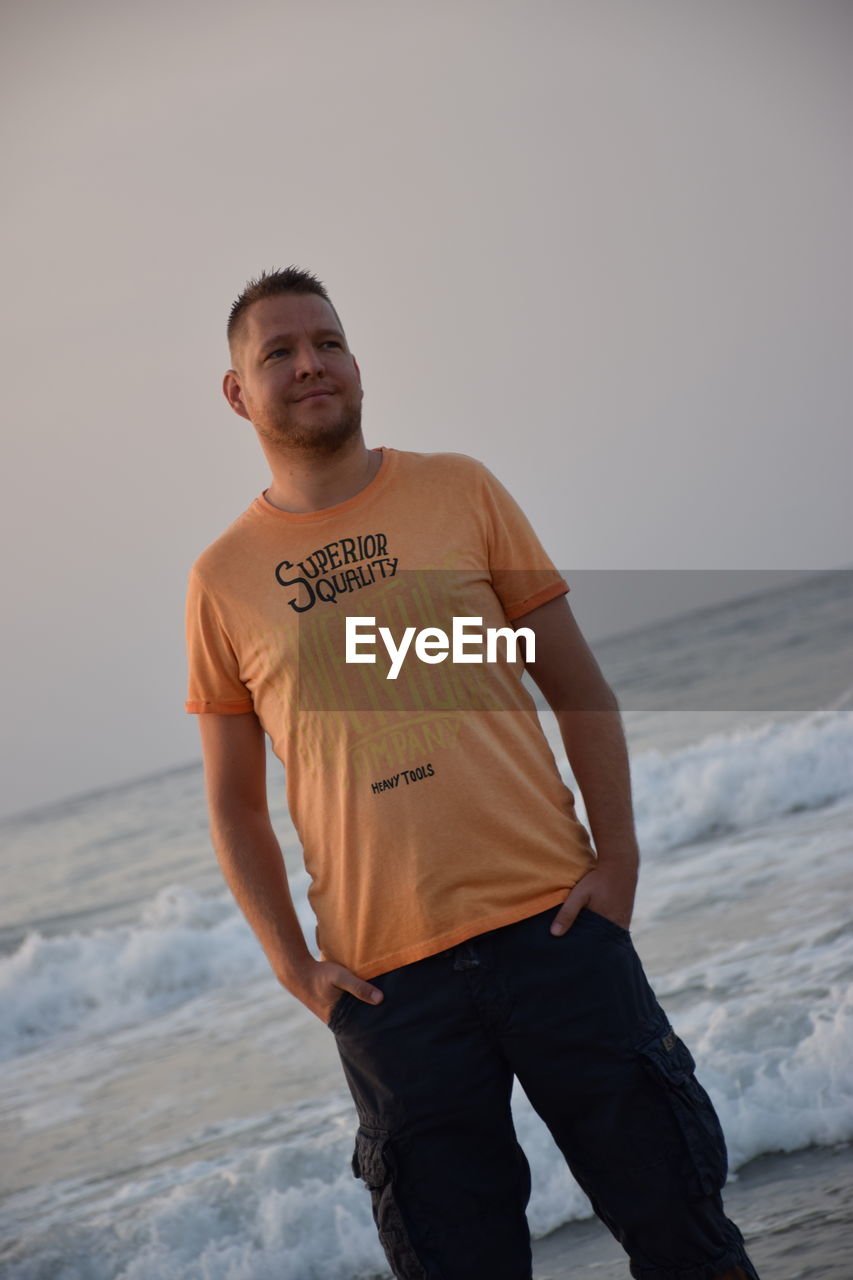 MAN STANDING ON BEACH AGAINST SKY