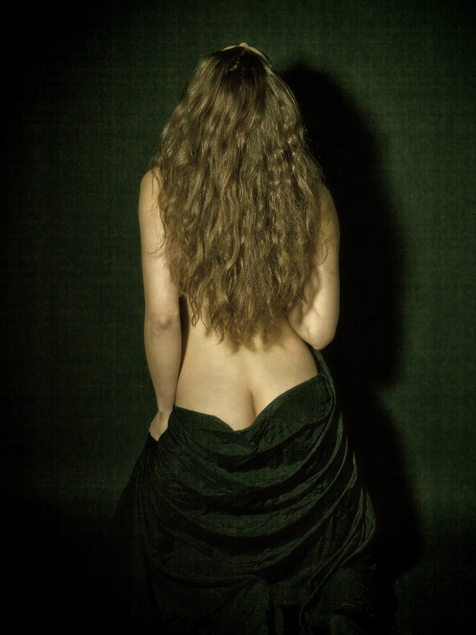 Rear view of sensuous naked woman holding black fabric while standing by wall