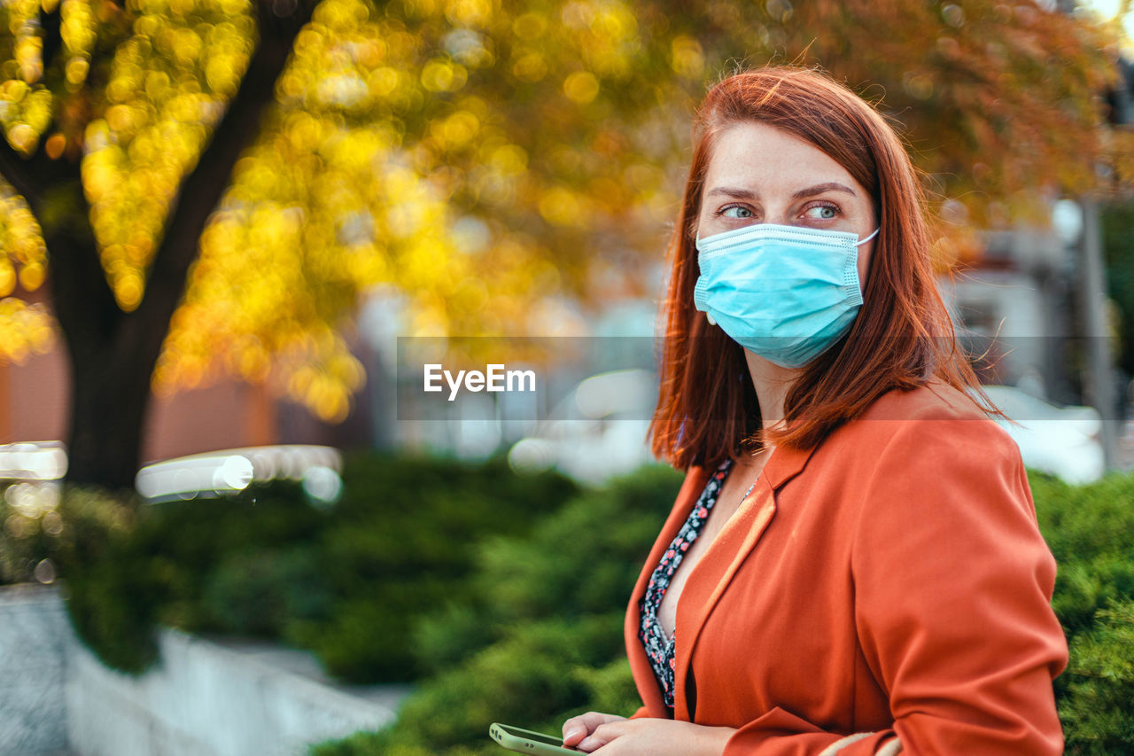 Beautiful woman wearing mask looking away while standing outdoors