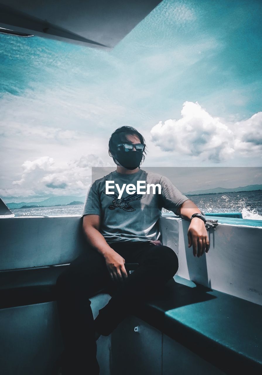 YOUNG MAN SITTING ON BOAT AGAINST SEA