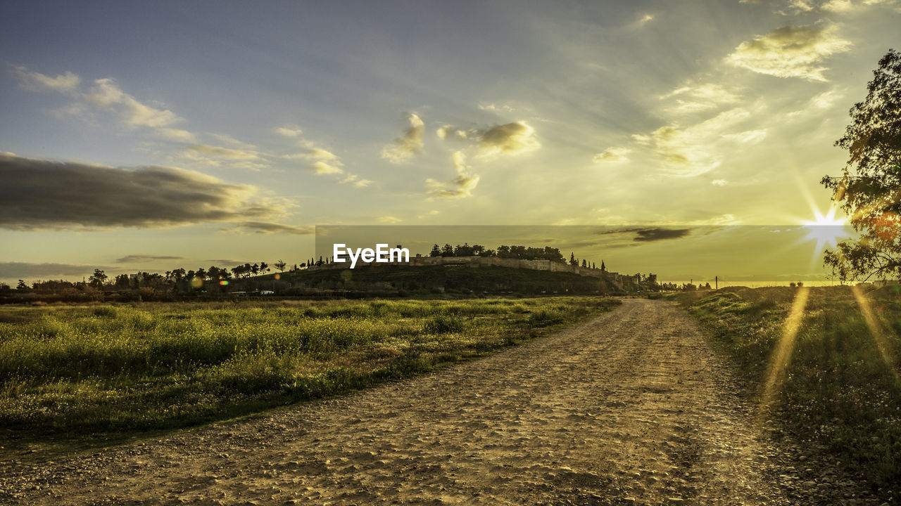 DIRT ROAD AMIDST FIELD AGAINST SKY