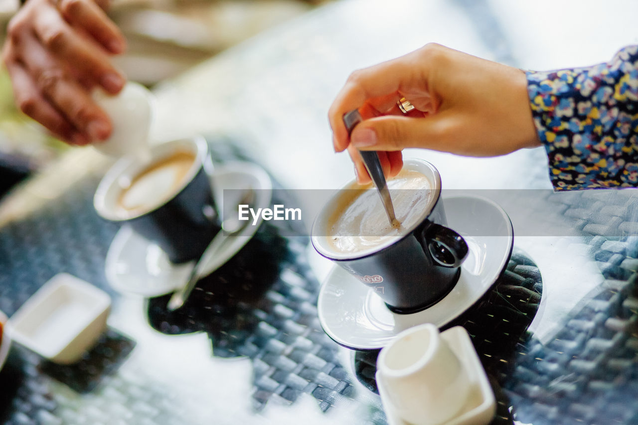 CLOSE-UP OF HAND POURING COFFEE CUP WITH TEA