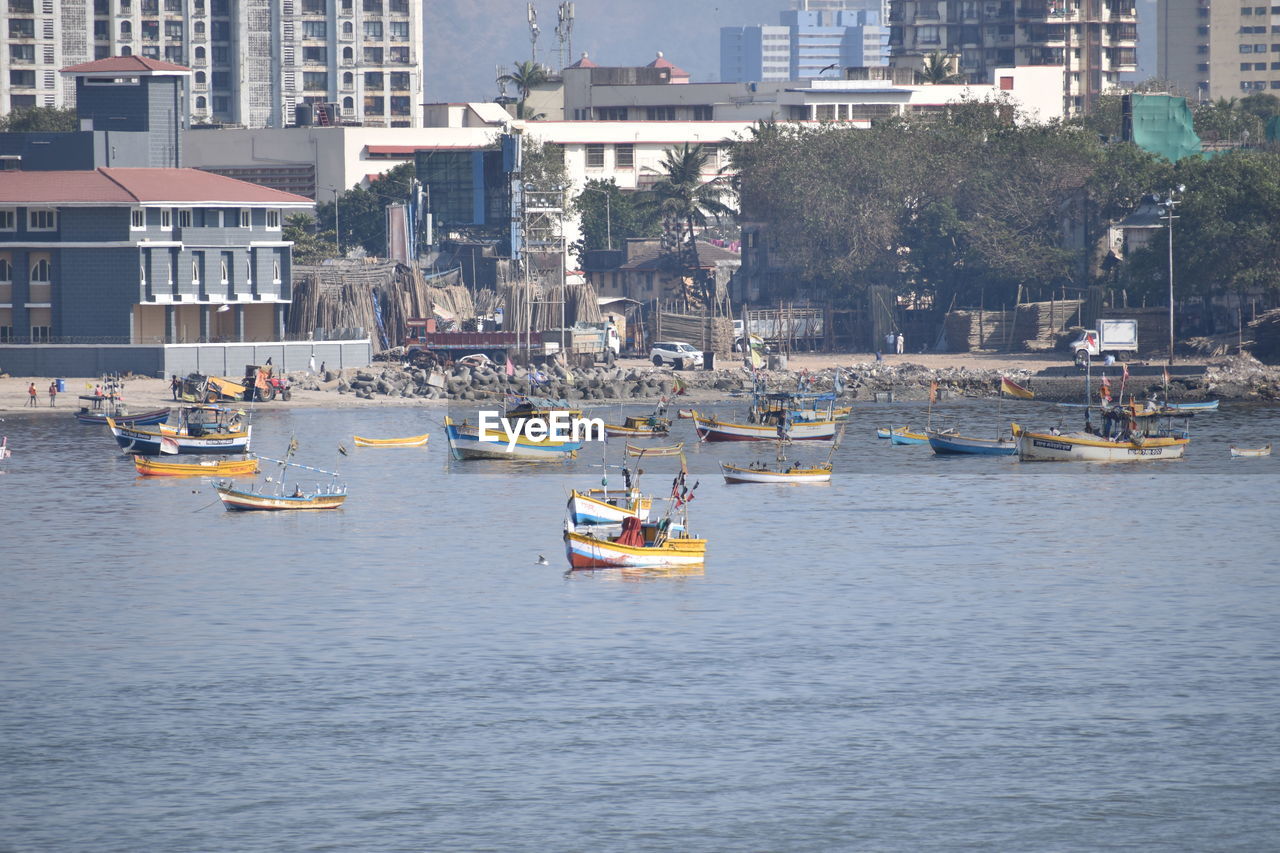 Sailboats sailing in sea against buildings in city