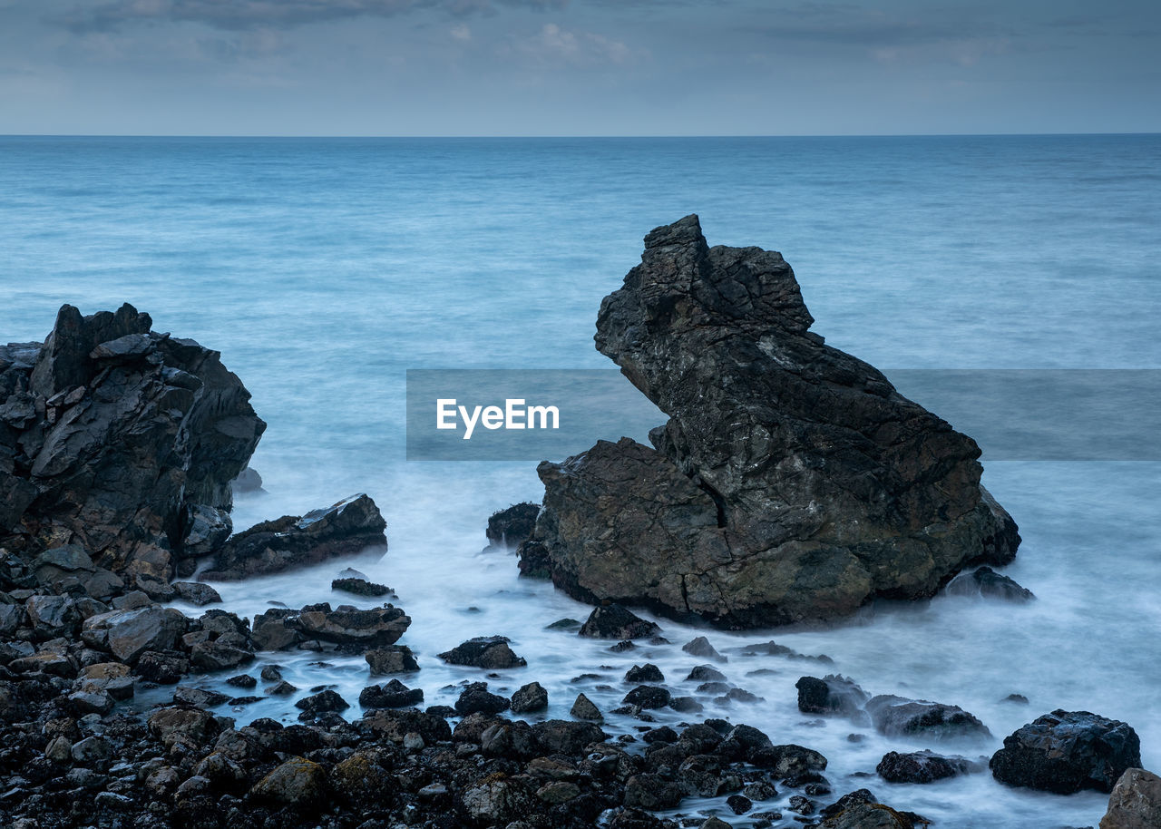 ROCK FORMATION ON SEA AGAINST SKY