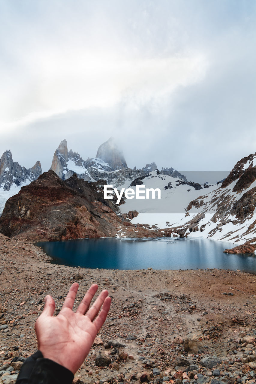 Midsection of person on snowcapped mountain against sky