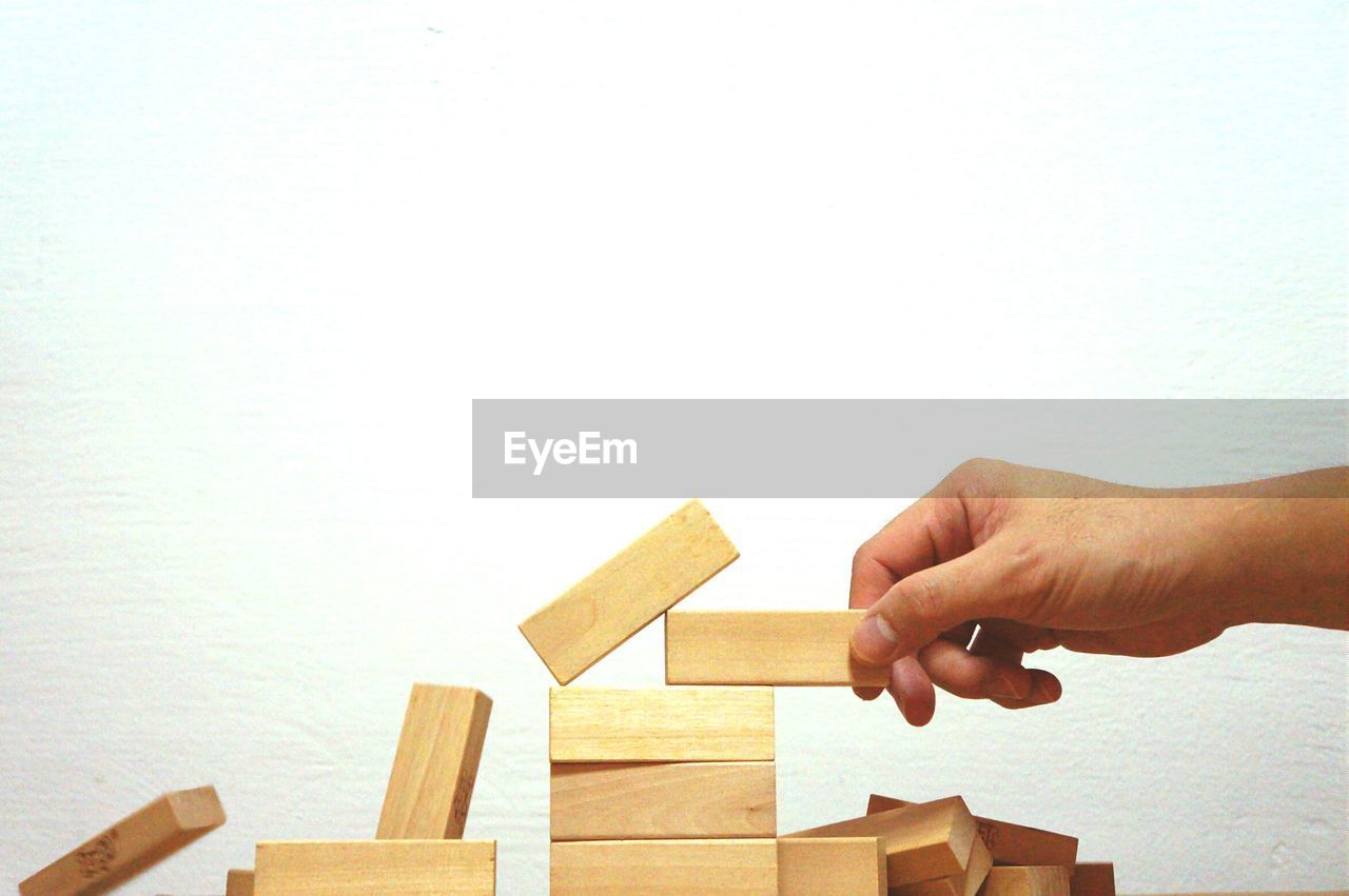 Cropped hand holding wooden block while playing game against white background