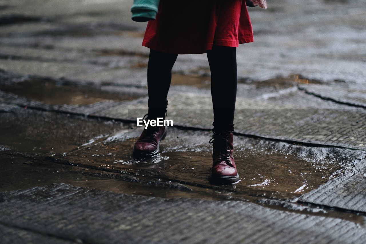 Low section of woman walking on puddle during rainy season