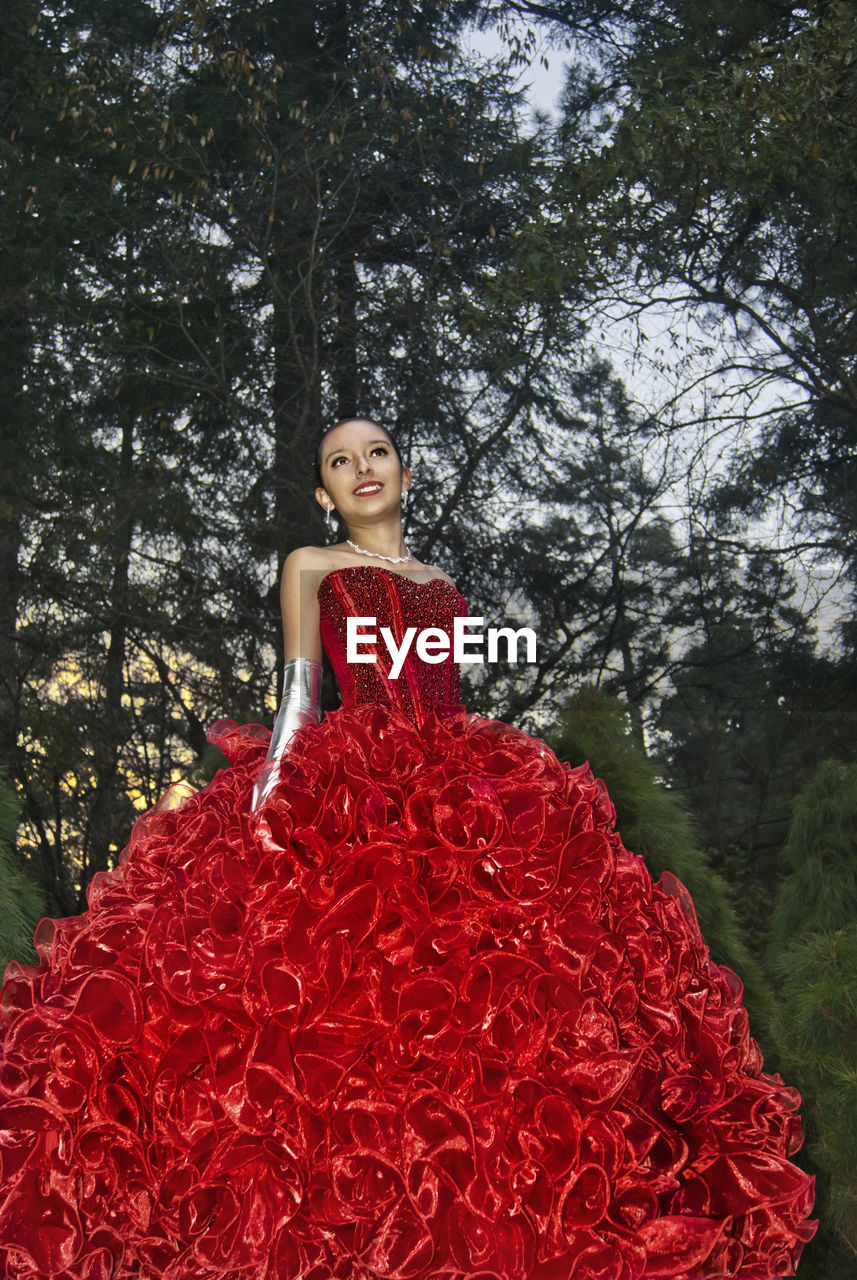 PORTRAIT OF SMILING YOUNG WOMAN STANDING ON TREE